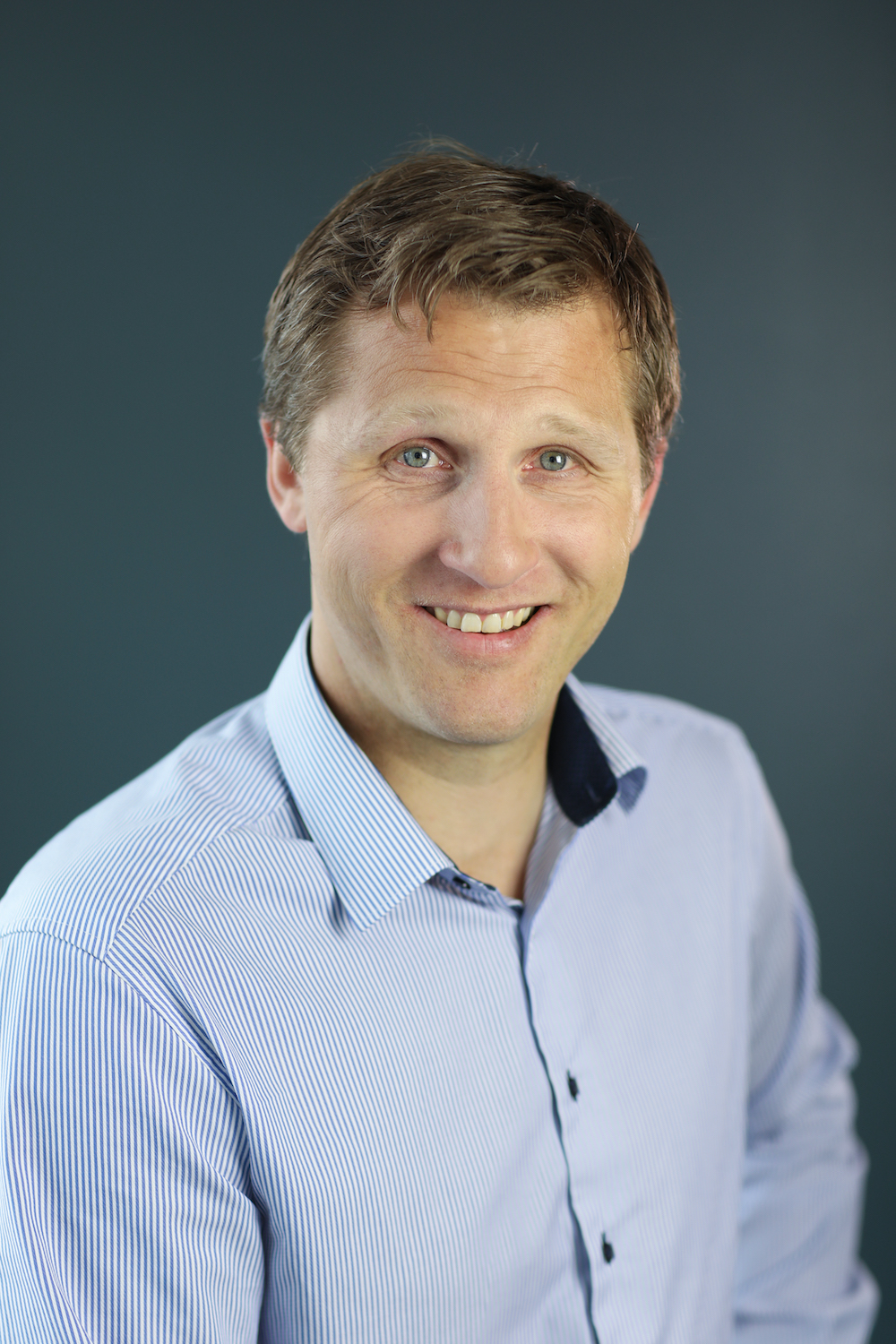 Profilbilde av Stian Green med blå skjorte på mørkegrå bakgrunn