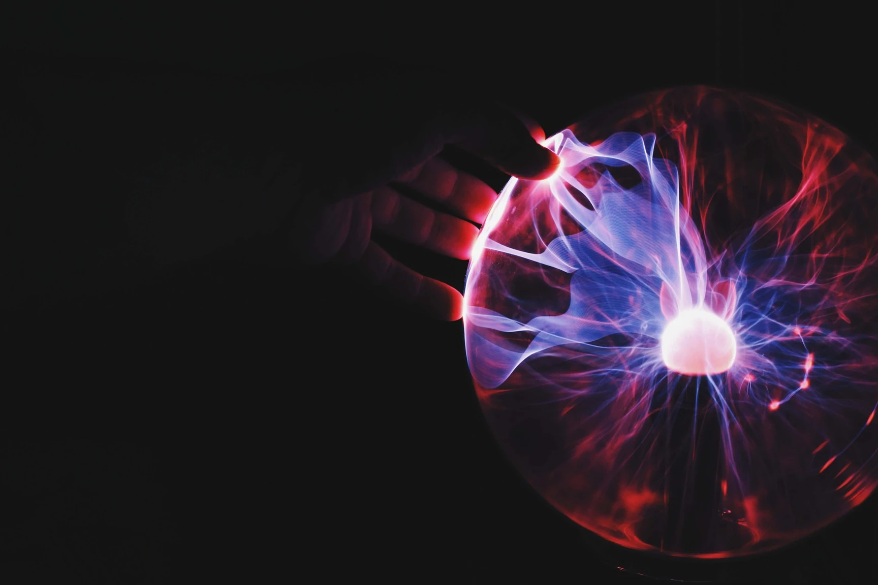 Hand touching a plasma ball with blue and red electric discharge streams radiating from a bright central point.