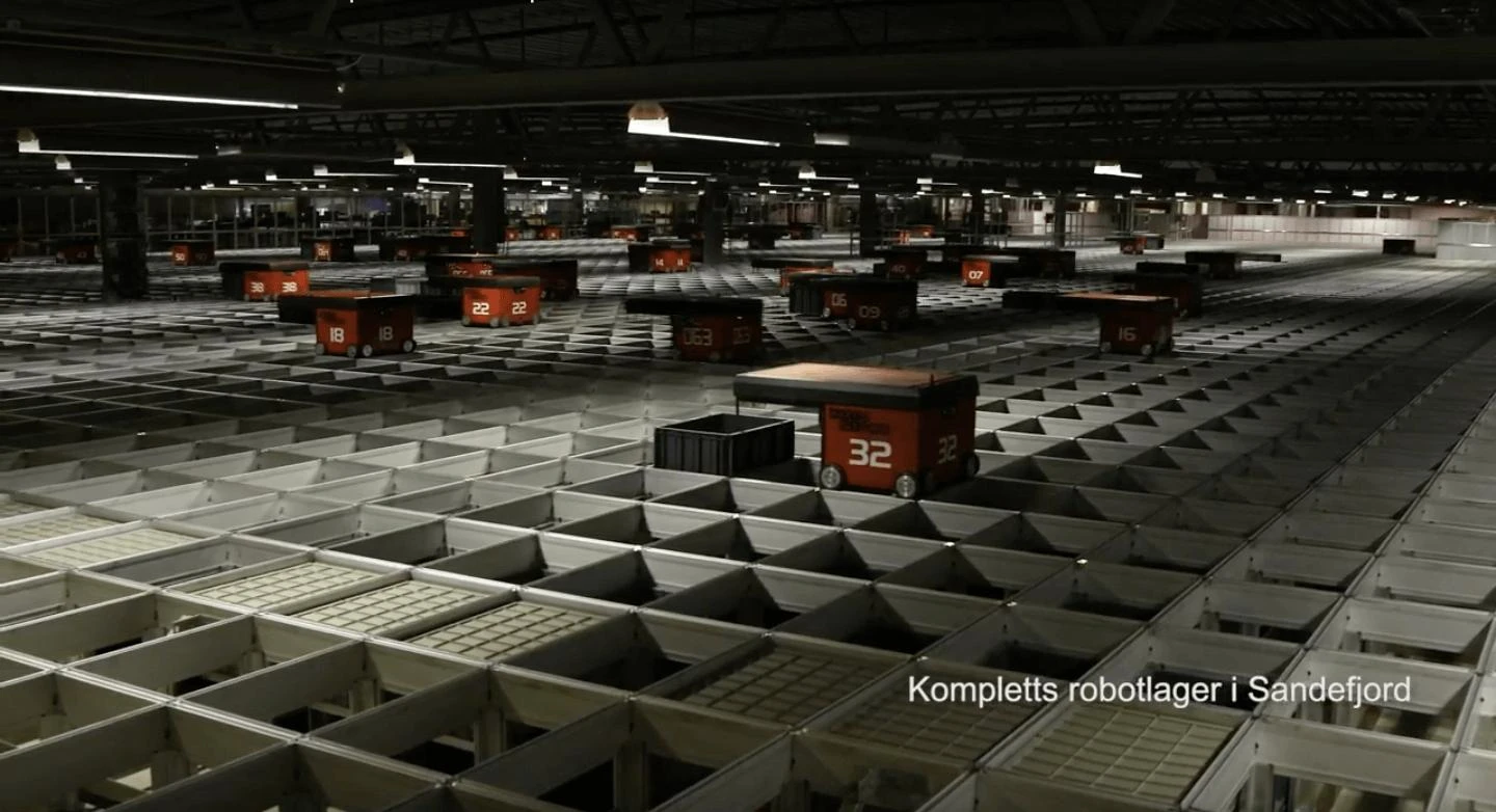 Large automated warehouse with numbered orange robots moving across a grid floor, from Komplett's facility in Sandefjord.