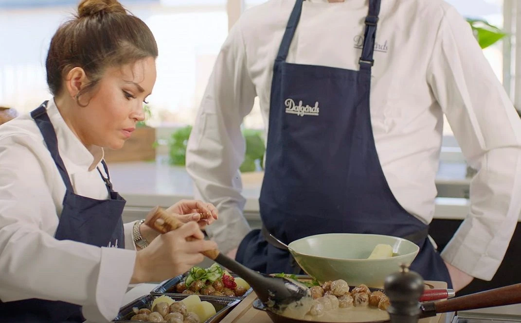 Two food workers in Dafgårds branded aprons preparing and plating dishes in a professional kitchen setting.