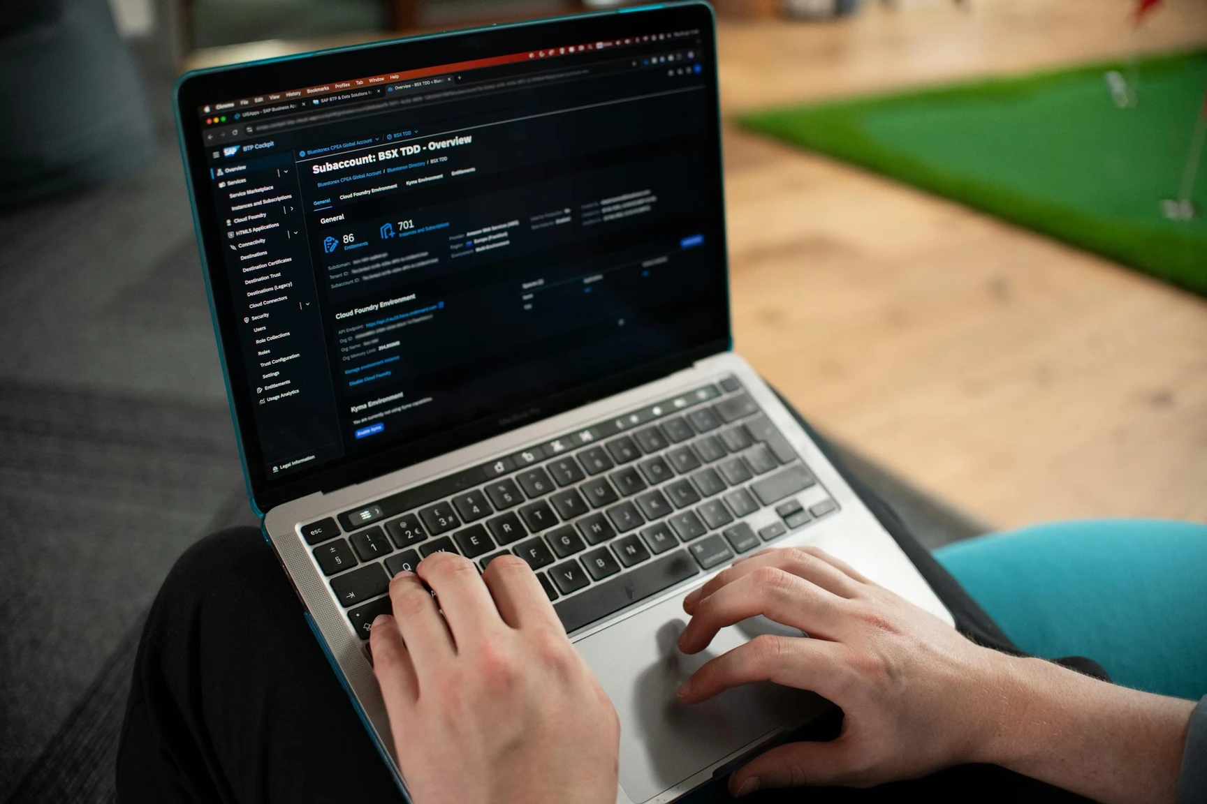 Person working on a laptop, viewing a dark-themed dashboard with technical details on the screen. A green putting mat is visible in the background.