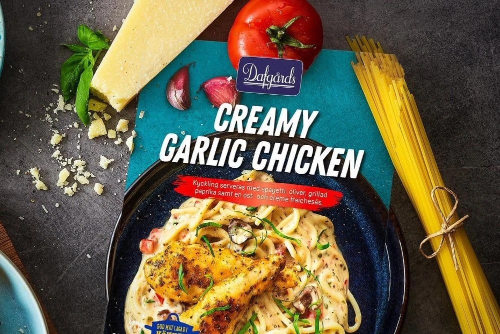 Dafgårds Creamy Garlic Chicken ready meal packaging displayed alongside fresh ingredients including tomato, garlic, and spaghetti.